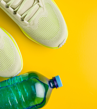 Turnschuhe und eine Trinkflasche vor gelbem Hintergrund